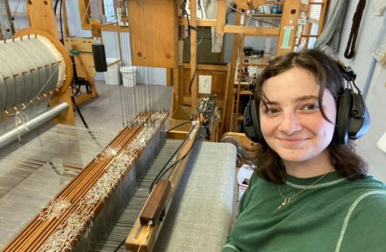 Rachel Obenhaus weaves on a 60-inch AVL Technical Computer-Dobby loom in Northport, Maine. She wears headphones to protect her ears from the loud pressurized air that shoots the shuttles of yarn back and forth.