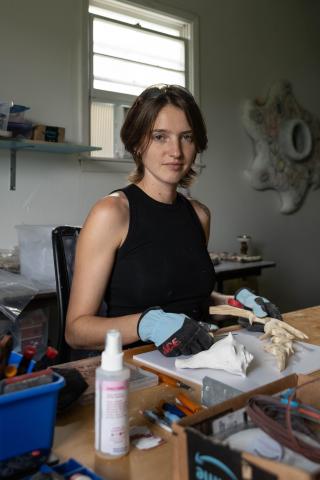 Headshot of Kenzie Wells carving wood in their home studio in Columbia, MO.