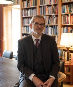 James A. van Dyke sitting on a table in front of a wall of books and a lamp