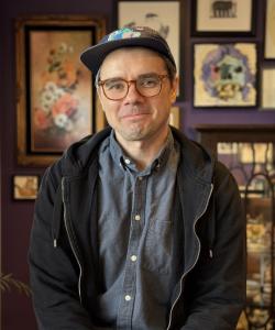 A middle-aged man with glasses and a baseball cap smiling.